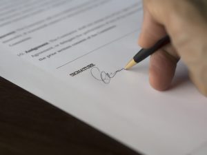 Podpisywanie dokumentu długopisem przy umowie na biurku.